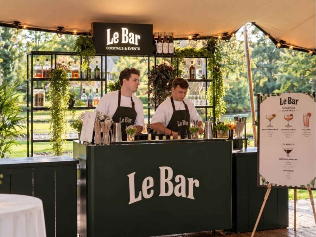 Twee bartenders van Le Bar achter een tentbar met signature cocktailmenu op een event
