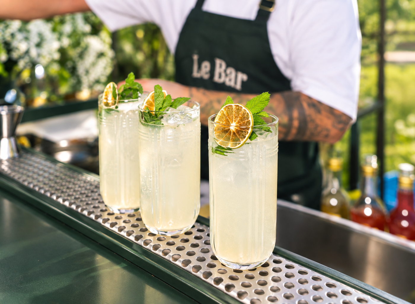 Drie Le Bar cocktails met munt en gedroogde limoen op de bar, bartender op de achtergrond